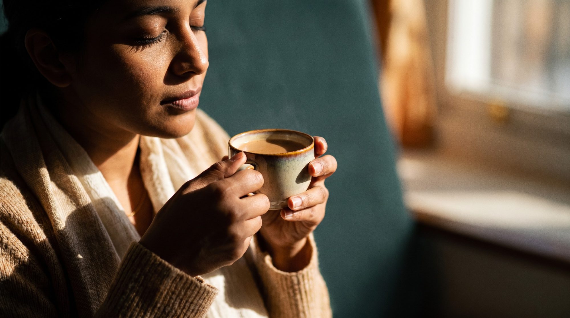 A woman holding a cup of chai with eyes closed, taking a slow calming breath