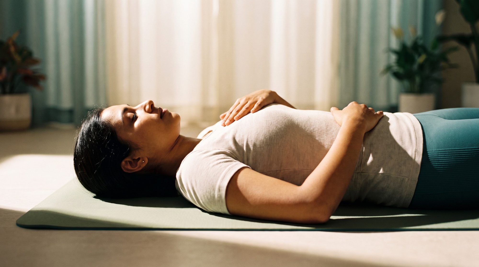 A woman resting on a mat at home with one hand on her chest and one on her belly