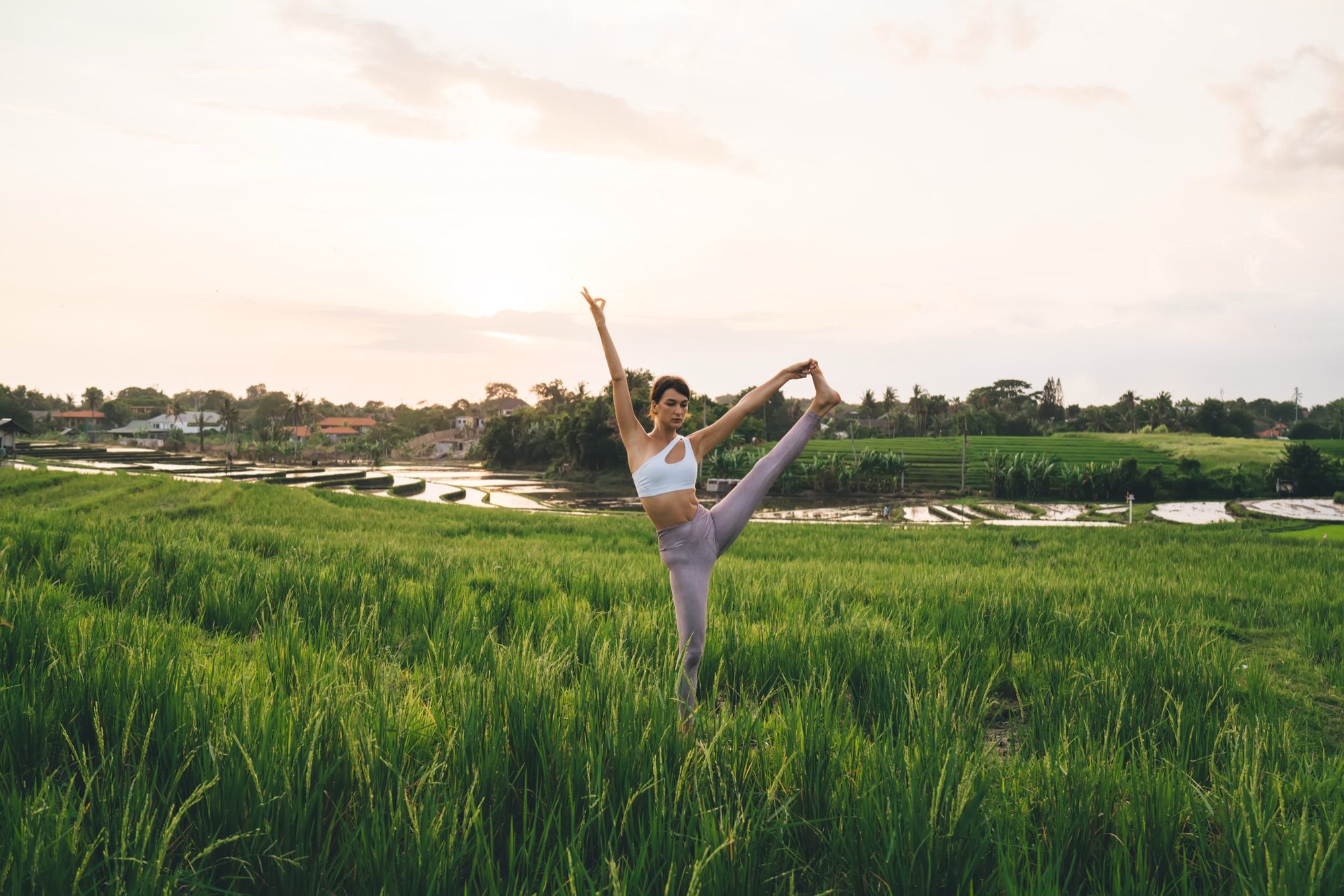 A woman practising yoga in a green field at sunrise — illustrative stock photography
