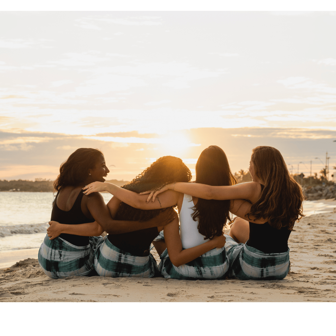 Four women hugging on the beach at sunset